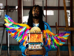 a person stands looking at the camera, holding a vibrant assemblage piece