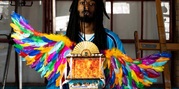 a person stands looking at the camera, holding a vibrant assemblage piece